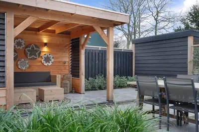 Image de The holiday home is located on a dead-end street in the beautiful, peaceful, and wooded park Jonkerstee with a spacious canopy featuring a lounge sofa.