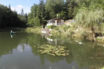 Image de Chalet surplombant un étang dans un cadre verdoyant.