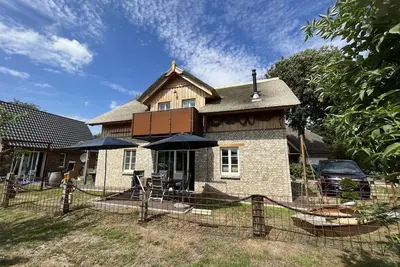 Image de maison de vacances au toit de chaume meublée individuellement et confortablement avec vue sur la baie, terrasse et balcon, espace barbecue et aire de jeux