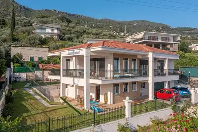 Image de εξοχική ισόγεια κατοικία σε κήπο με γκαζόν με θέα θάλασσα και καταπράσινο λόφο