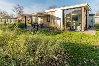 Image de Ce chalet est entouré d'un jardin abrité avec des dunes, de l'ammophile et une rangée d'arbres. Litt